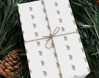 Op de afbeelding: Verpakt cadeau met wit cadeaupapier met een herhaald patroon van een beer met een hoed en de tekst "Merry Making Co." Het cadeau is vastgebonden met touw en geplaatst tegen een achtergrond van dennennaalden en een dennenappel.