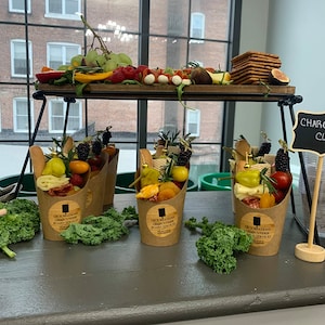 Pode incluir: Quatro caixas individuais de charcutaria com uma sele&ccedil;&atilde;o de carnes, queijos, frutas e vegetais. As caixas s&atilde;o de papel castanho e t&ecirc;m um autocolante que diz "Occasions Charcuterie Board Services".