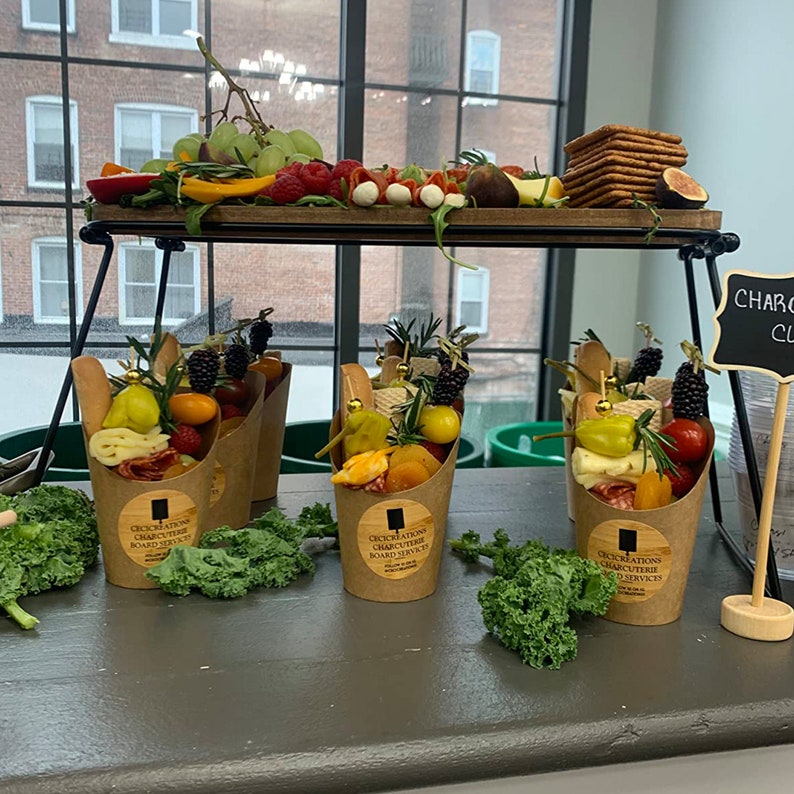 Pode incluir: Quatro caixas individuais de charcutaria com uma sele&ccedil;&atilde;o de carnes, queijos, frutas e vegetais. As caixas s&atilde;o de papel castanho e t&ecirc;m um autocolante que diz "Occasions Charcuterie Board Services".