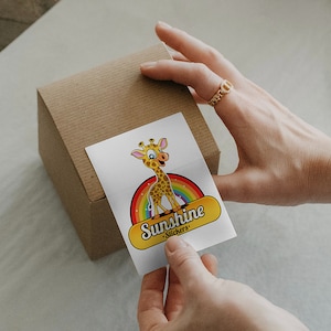 Pode incluir: Um adesivo branco com uma girafa de desenho animado em p&eacute; em um arco-&iacute;ris. O adesivo diz "Sunshine Stickers" em texto amarelo.