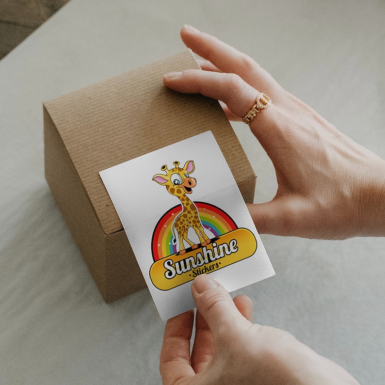Pode incluir: Um adesivo branco com uma girafa de desenho animado em p&eacute; em um arco-&iacute;ris. O adesivo diz "Sunshine Stickers" em texto amarelo.