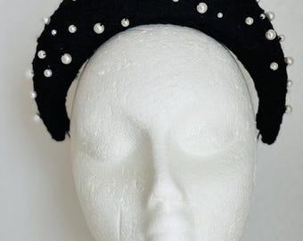 May include: A black headband with white pearl embellishments. The headband is curved and has a wide, padded band.