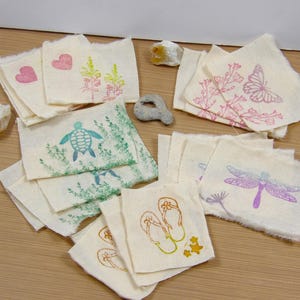 May include: A collection of 10 fabric squares with various hand-stamped designs, including a turtle, a dragonfly, flowers, hearts, and flip-flops. The fabric squares are all white with a natural linen texture.
