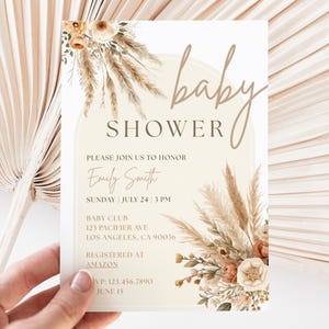 May include: Baby shower invitation with floral and pampas grass accents. The invitation features the words "baby shower" in a script font, along with details for the event, including the honoree's name, date, time, and location.