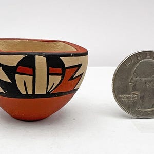 May include: A small, hand-painted pottery bowl with a geometric design in black, red, and white. The bowl is about the size of a quarter.