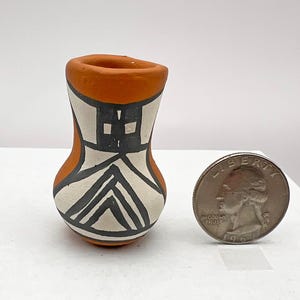 May include: A small, hand-painted pottery vase with a geometric design in black and white on a terracotta background. The vase is about the size of a US quarter.