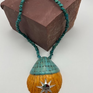 May include: A turquoise and orange shell pendant necklace with a silver starburst design. The necklace is made of turquoise beads and has a silver clasp.