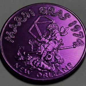 May include: A circular purple Mardi Gras 1979 New Orleans coin featuring a raised relief design of a winged figure playing a flute, a geometric shape, and a staff. The text Mardi Gras 1979 and New Orleans is embossed along the coin's edge.