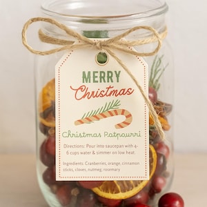 May include: A glass jar filled with festive Christmas potpourri, featuring cranberries, orange slices, and cinnamon sticks. The jar has a tag with "Merry Christmas" and "Christmas Potpourri" tied with twine.