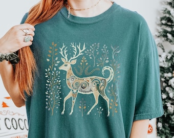 Puede incluir: Camiseta de gran tamaño azul turquesa con un gráfico de reno estampado en dorado y blanco. El reno está rodeado de elementos florales estilizados.
