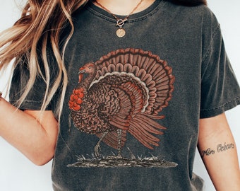Puede incluir: Una camiseta gris oscuro con una ilustración vintage de un pavo. El pavo es marrón y rojo con un diseño detallado. La camiseta tiene cuello redondo y mangas cortas.