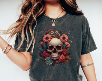 Könnte beinhalten: Ein dunkelgraues T-Shirt mit einem Schädel, der von bunten Blumen umgeben ist. Der Schädel ist weiß mit schwarzen Augenhöhlen und einer schwarzen Nase. Die Blumen sind rot, rosa, blau und grün.