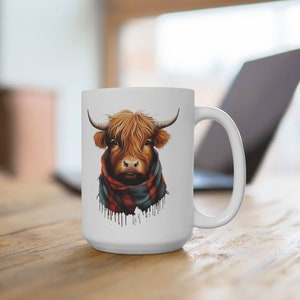 Pode incluir: Caneca de cer&acirc;mica branca com uma ilustra&ccedil;&atilde;o de uma vaca Highland. A vaca tem pelo castanho, chifres e um cachecol xadrez vermelho e preto. A caneca est&aacute; sobre uma superf&iacute;cie de madeira.