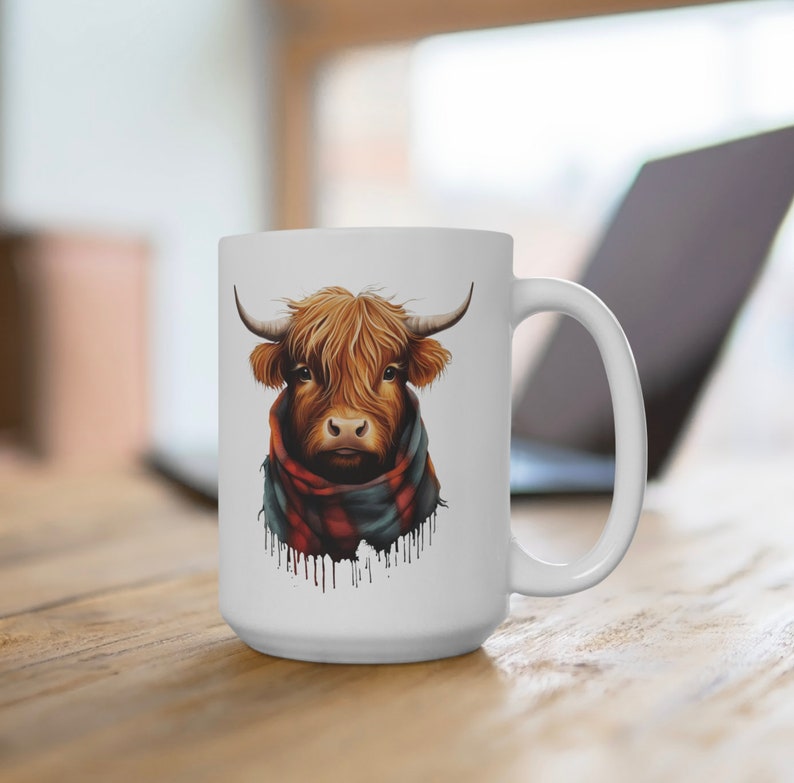 Pode incluir: Caneca de cer&acirc;mica branca com uma ilustra&ccedil;&atilde;o de uma vaca Highland. A vaca tem pelo castanho, chifres e um cachecol xadrez vermelho e preto. A caneca est&aacute; sobre uma superf&iacute;cie de madeira.