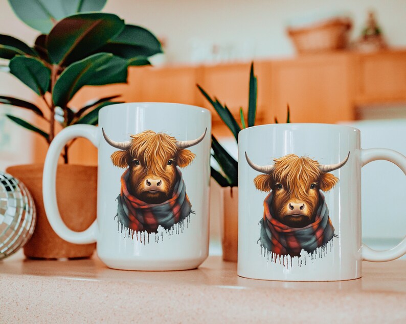 Pode incluir: Duas canecas de cer&acirc;mica branca com um design de vaca das Terras Altas. A vaca tem pelo castanho, chifres grandes e usa um cachecol xadrez vermelho e preto. As canecas est&atilde;o em uma superf&iacute;cie rosa claro.