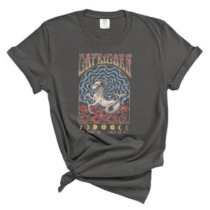 May include: A dark gray t-shirt with a vintage-style graphic of a Capricorn zodiac sign. The graphic features a goat with a floral design and the text "Capricorn" and "Dec 22 - Jan 19".