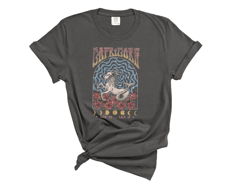 May include: A dark gray t-shirt with a vintage-style graphic of a Capricorn zodiac sign. The graphic features a goat with a floral design and the text "Capricorn" and "Dec 22 - Jan 19".