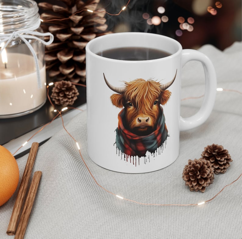 Pode incluir: Caneca de cer&acirc;mica branca com uma ilustra&ccedil;&atilde;o de uma vaca das Terras Altas. A vaca tem pelo castanho, chifres e um cachecol xadrez vermelho e azul. A caneca est&aacute; cheia de l&iacute;quido escuro.