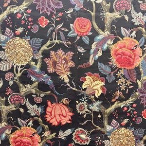 May include: A dark fabric with a detailed floral pattern. The design features large, colorful flowers in shades of red, yellow, and purple, along with green leaves and branches. The background is black.