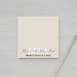May include: A beige card with the text "Board Certified Behaviour Analyst" and the acronym "BCBA" in large white letters. The text "Michelle Hanes, M.A., BCBA" is printed below the acronym.