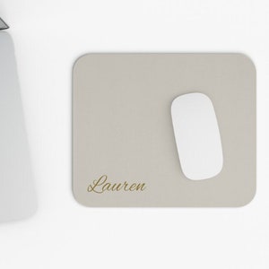May include: A light grey mouse mat with the name "Lauren" written in gold script. A white computer mouse is on the mat.