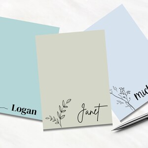 May include: Three blank notepads with different coloured backgrounds and personalised names: Logan, Janet, and Michelle. The notepad with the name Logan has a wave design at the bottom. The notepad with the name Janet has a floral design. The notepad with the name Michelle has a floral design.
