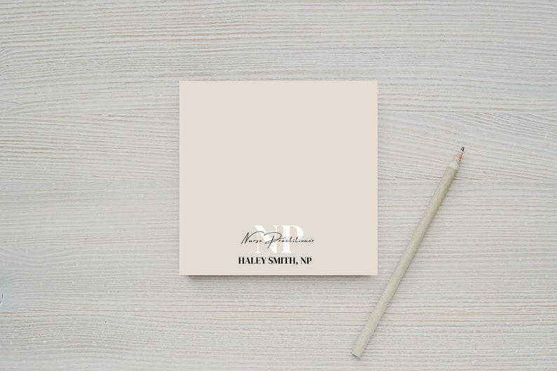 May include: A beige notepad with the text "Nurse Practitioner" and "HALEY SMITH, NP" printed on it. A pencil is lying on a white wooden surface next to the notepad.