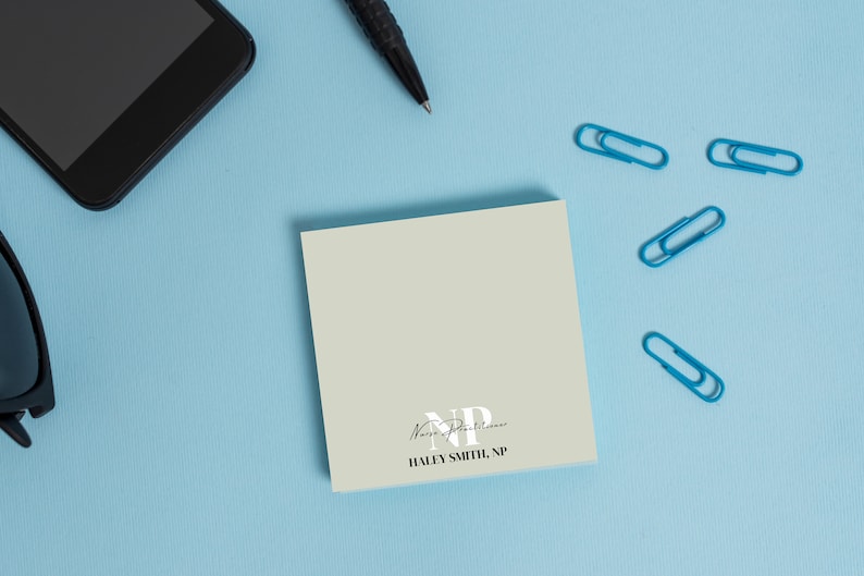 May include: A light green notepad with the text "Nurse Practitioner" and "HALEY SMITH, NP" printed on it. The notepad is on a light blue surface with a black cell phone, a black pen, and four blue paper clips.