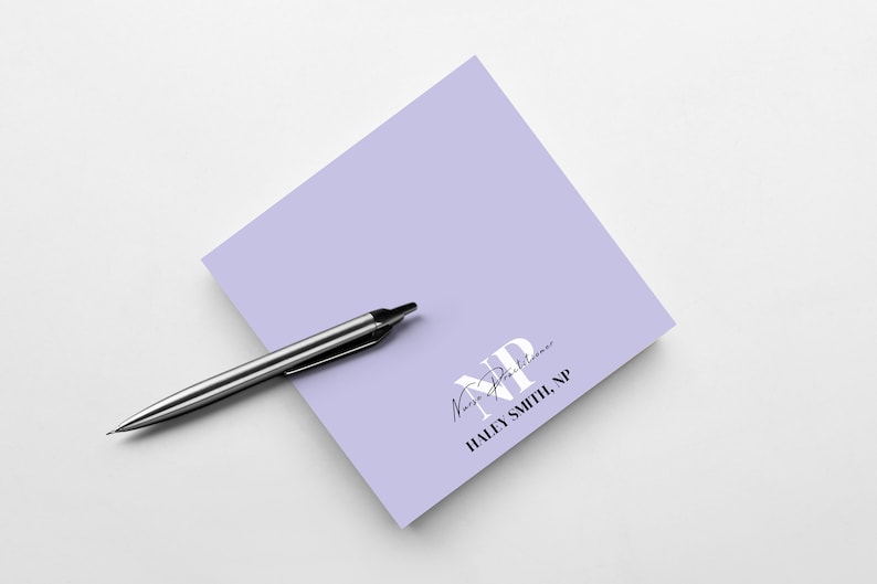 May include: A lavender notepad with the text "Nurse Practitioner" and "HALEY SMITH, NP" in black text. A silver pen is lying on top of the notepad.