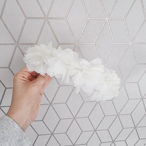 May include: A white flower crown made of fabric flowers. The crown is made of many small, delicate flowers.