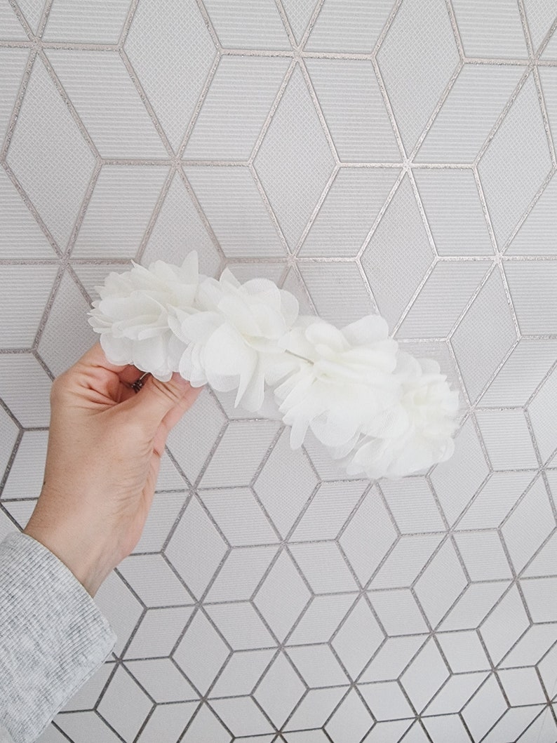 May include: A white flower crown made of fabric flowers. The crown is made of many small, delicate flowers.