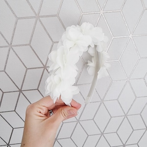 May include: White flower headband with a white elastic band. The headband is made of fabric flowers.