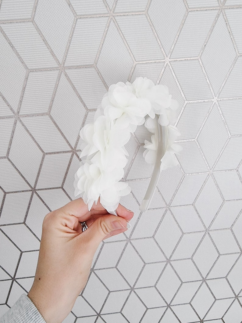 May include: White flower headband with a white elastic band. The headband is made of fabric flowers.