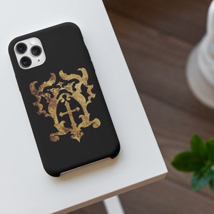 May include: A black phone case with a gold-colored crest featuring a cross and intricate details. The crest has a distressed, aged look.