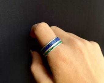 May include: A silver ring with a blue and green inlay. The ring is wide and has a flat top.