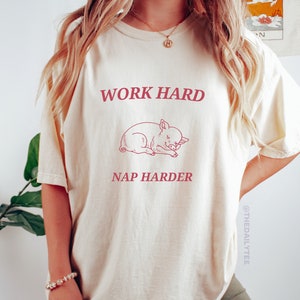 May include: Ivory t-shirt with the text "Work Hard Nap Harder" and a sleeping pig illustration.