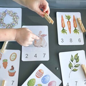 Op de afbeelding: Een set van zes Pasen-thema tellen kaarten met kleurrijke afbeeldingen van een krans, konijn, wortels, bladeren, eieren en bloemen. Elke kaart heeft een nummerrooster met de nummers 1 tot en met 9. De kaarten zijn ontworpen voor kinderen om te leren tellen en nummers te herkennen.