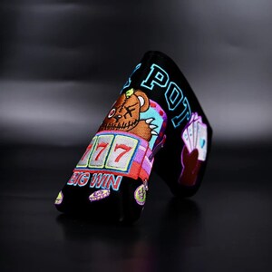 May include: Black golf club head cover with a colorful embroidered design featuring a teddy bear, slot machine, playing cards, and the text "BIG WIN" and "BIG POT".