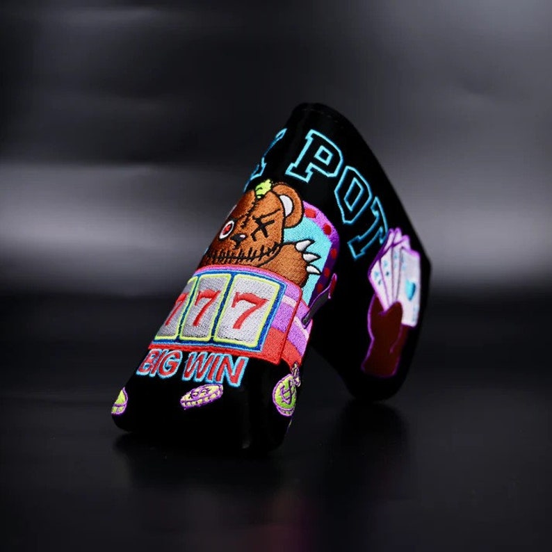 May include: Black golf club head cover with a colorful embroidered design featuring a teddy bear, slot machine, playing cards, and the text "BIG WIN" and "BIG POT".