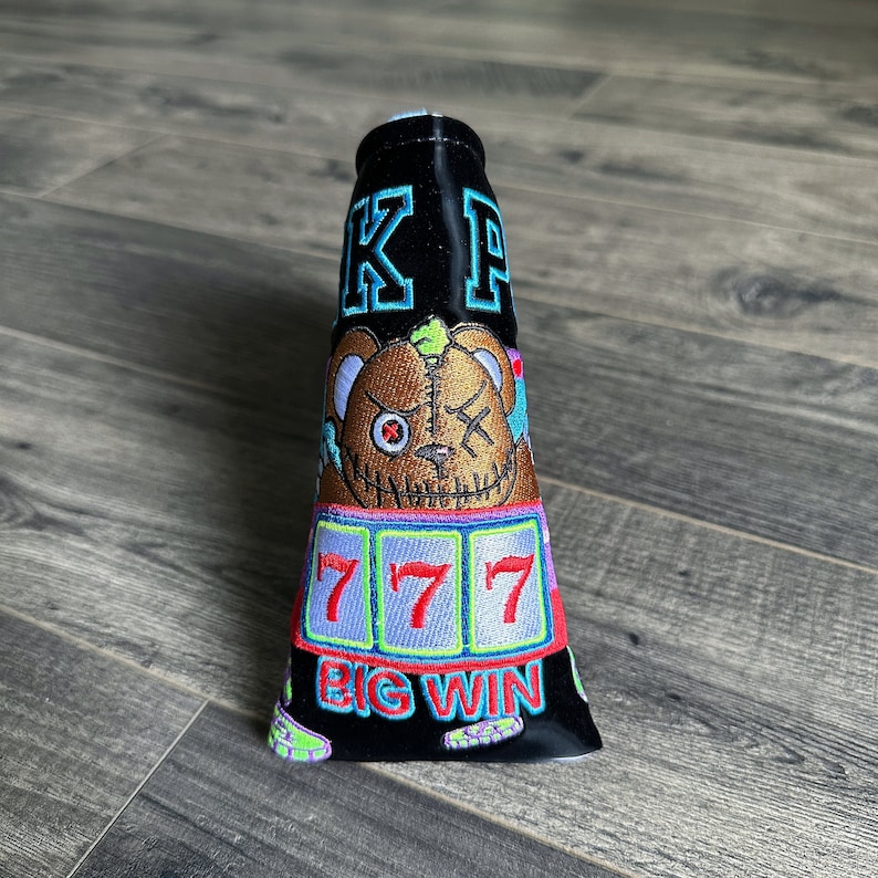 May include: Black golf club head cover with a cartoon bear face, slot machine with 777 and the words "BIG WIN" embroidered on it. The cover has the initials "KP" embroidered on the top.
