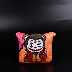 May include: Embroidered patch featuring a bear character dressed as a clown with green hair, red suit, and a cigarette. The patch has a pink and orange background with the word "HA" repeated. The bear has a painted face with a winking eye.