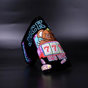 May include: Black golf club head cover with a colorful embroidered design of a cartoon bear with a slot machine showing 777 and the text "BIG WIN". The text "JACK" is also embroidered on the cover.