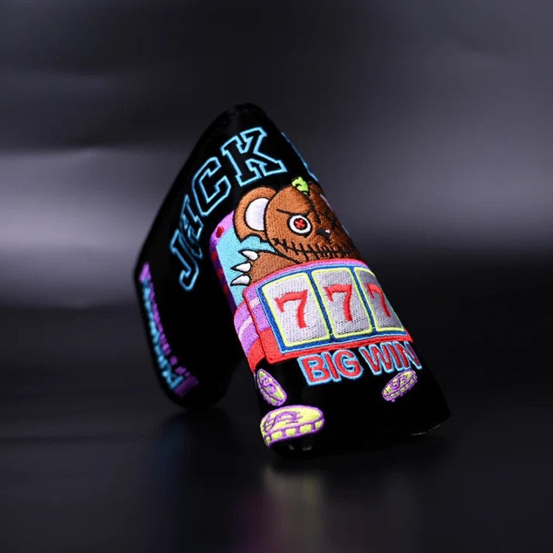 May include: Black golf club head cover with a colorful embroidered design of a cartoon bear with a slot machine showing 777 and the text "BIG WIN". The text "JACK" is also embroidered on the cover.