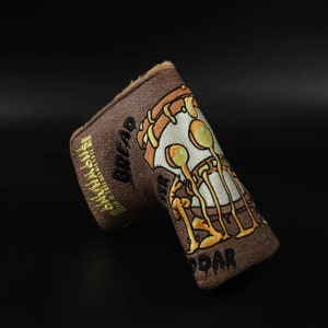May include: Brown golf club head cover with a cartoon skull design. The skull is wearing a hat and has a dripping egg yolk on its head. The text "DEAD" and "ROAR" are embroidered on the cover.