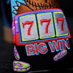 May include: A black and blue embroidered patch with a slot machine design. The slot machine shows three red sevens and the words "BIG WIN" in red and blue.