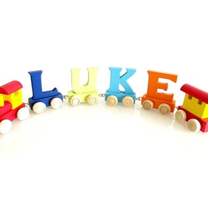 May include: A wooden toy train with colourful letters spelling out the name "LUKE". The train has a red engine, a yellow caboose, and letter cars in blue, green, light blue, and orange.