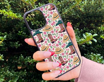 May include: A black phone case with a white background and a pattern of pink flowers, cowboy boots, and cowboy hats.