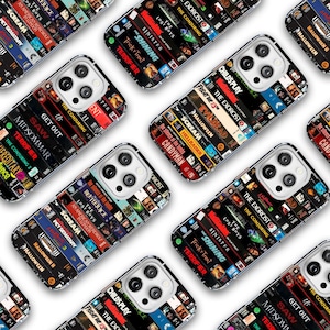 May include: Multiple phone cases with a design of stacked VHS tapes featuring horror movie titles like "The Exorcist," "Halloween," and "Scream." The cases have a clear border and a glossy finish, with the phone's camera visible.