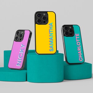 Pode incluir: Três capas de telefone personalizadas com nomes diferentes. As capas são amarelas, rosa e azuis com contornos pretos. Os nomes são "Samantha", "Nicky" e "Charlotte".