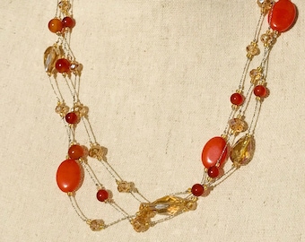 May include: Multi-strand necklace with orange and gold beads. The necklace features a layered design with various sized beads, including round and oval shapes.